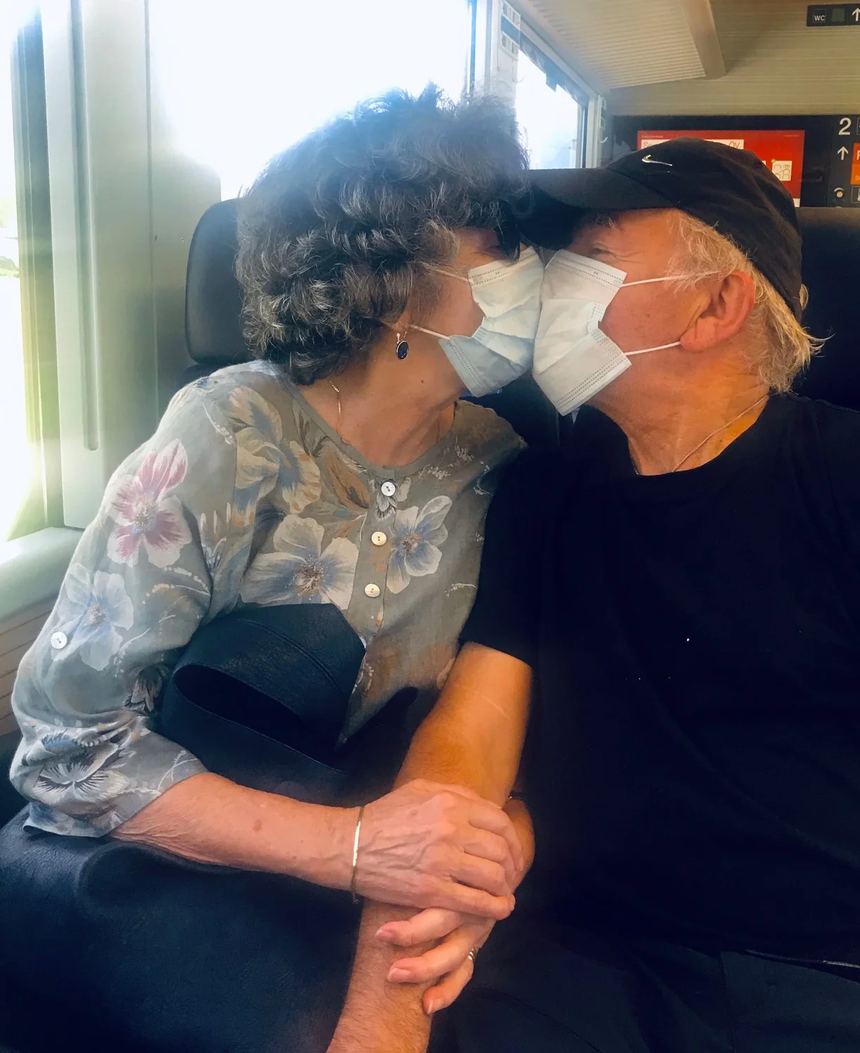 Ein älteres Ehepaar küsst sich im Zug mit Maske zu Coronazeit. Steht für den Blogbeitrag: Maskenpflicht und Nähe und Distanz.
