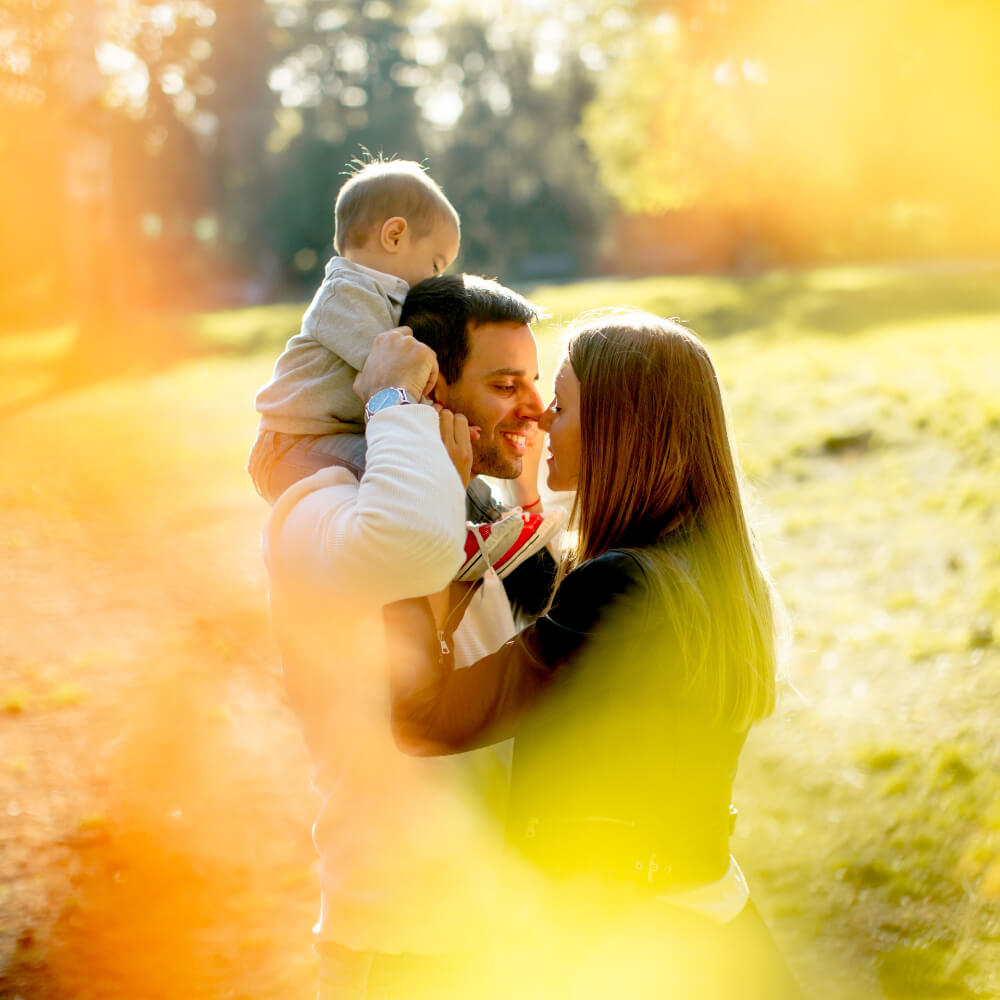 Ein Mann mit Kind auf den Schultern wendet sich liebevoll seiner Frau und Mutter seines Kindes zu. Ein Paartherapie - Angebot für Paare die auch Eltern sind.