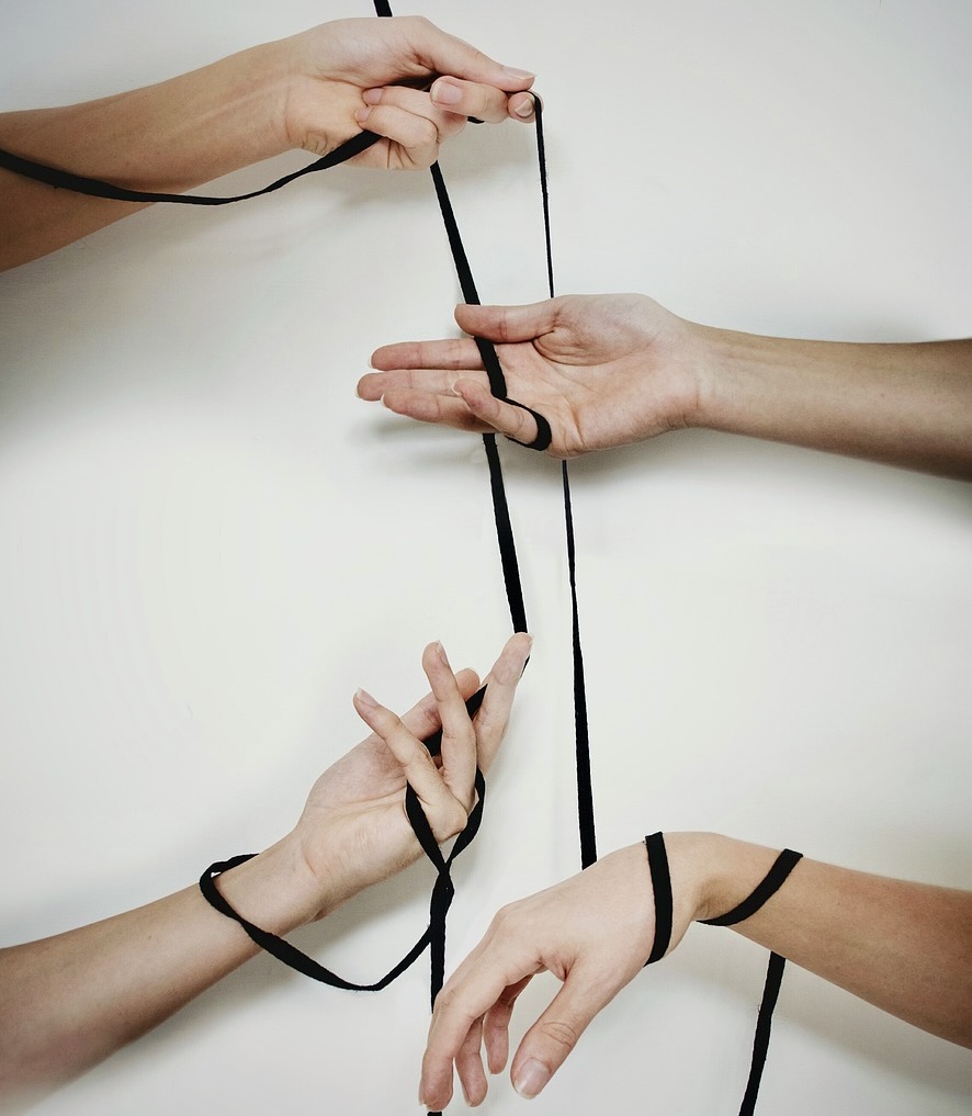 Vier Hände die mit einer Schnur verstrickt und verbunden sind. Soll aufzeigen, dass es in Mediationen und Teamkonflikten oft Abhängigkeiten gibt und Verstrickungen gibt. Diese gilt es unter anderem zu lösen.